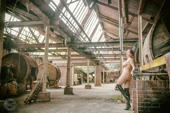 naakte vrouw in een oude industriele ruimte leunt ontspannen tegen een machine. Naaktfotografie door Your Naked Skin